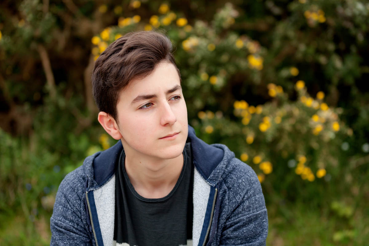 Attractive teenager guy in a park with green plants of background