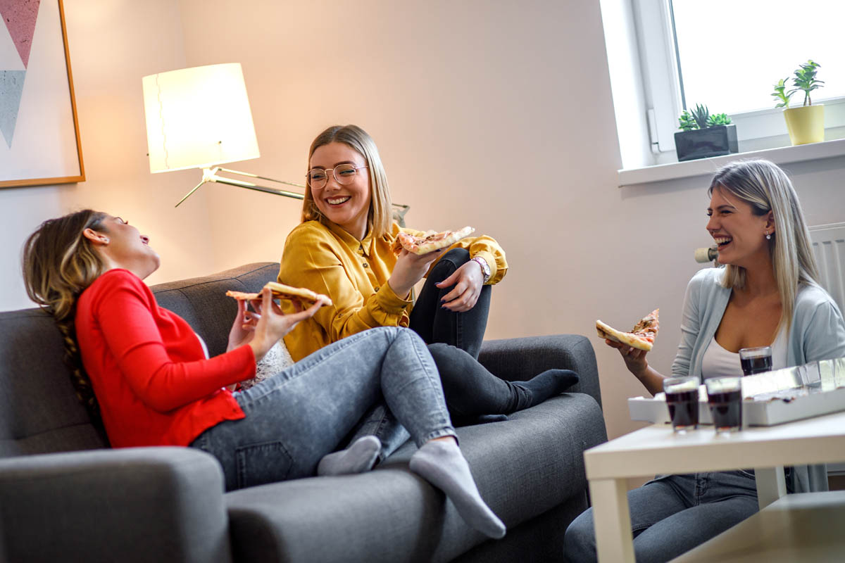 Three female friends chatting and enjoying eating pizza at home.