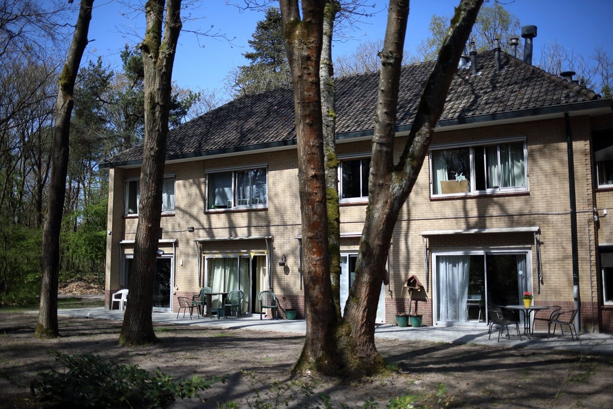 Achterkant van het woongebouw met terrassen grenzend aan het bos, voorzien van tuinmeubilair voor bewoners.