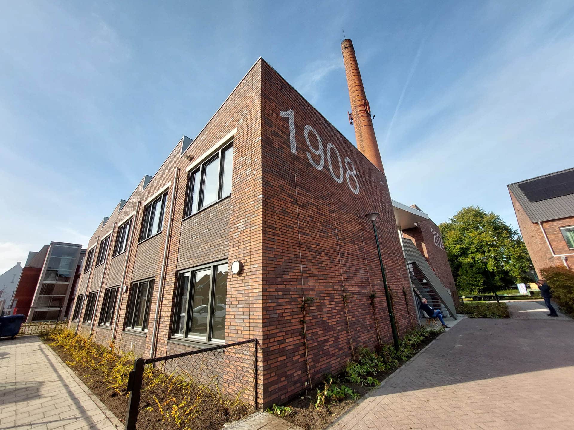 Buitenaanzicht van een modern bakstenen gebouw met het jaartal 1908 op de gevel.
