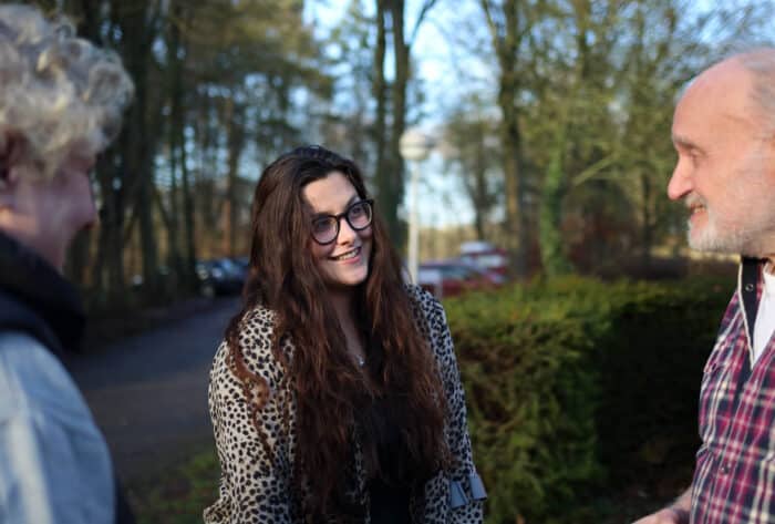 Twee mensen staan buiten met elkaar in gesprek in een groene omgeving.