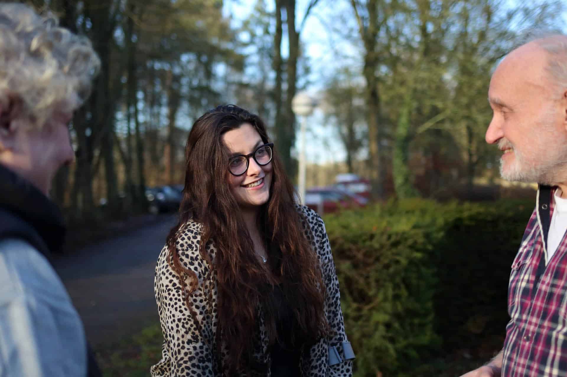 Twee mensen staan buiten met elkaar in gesprek in een groene omgeving.