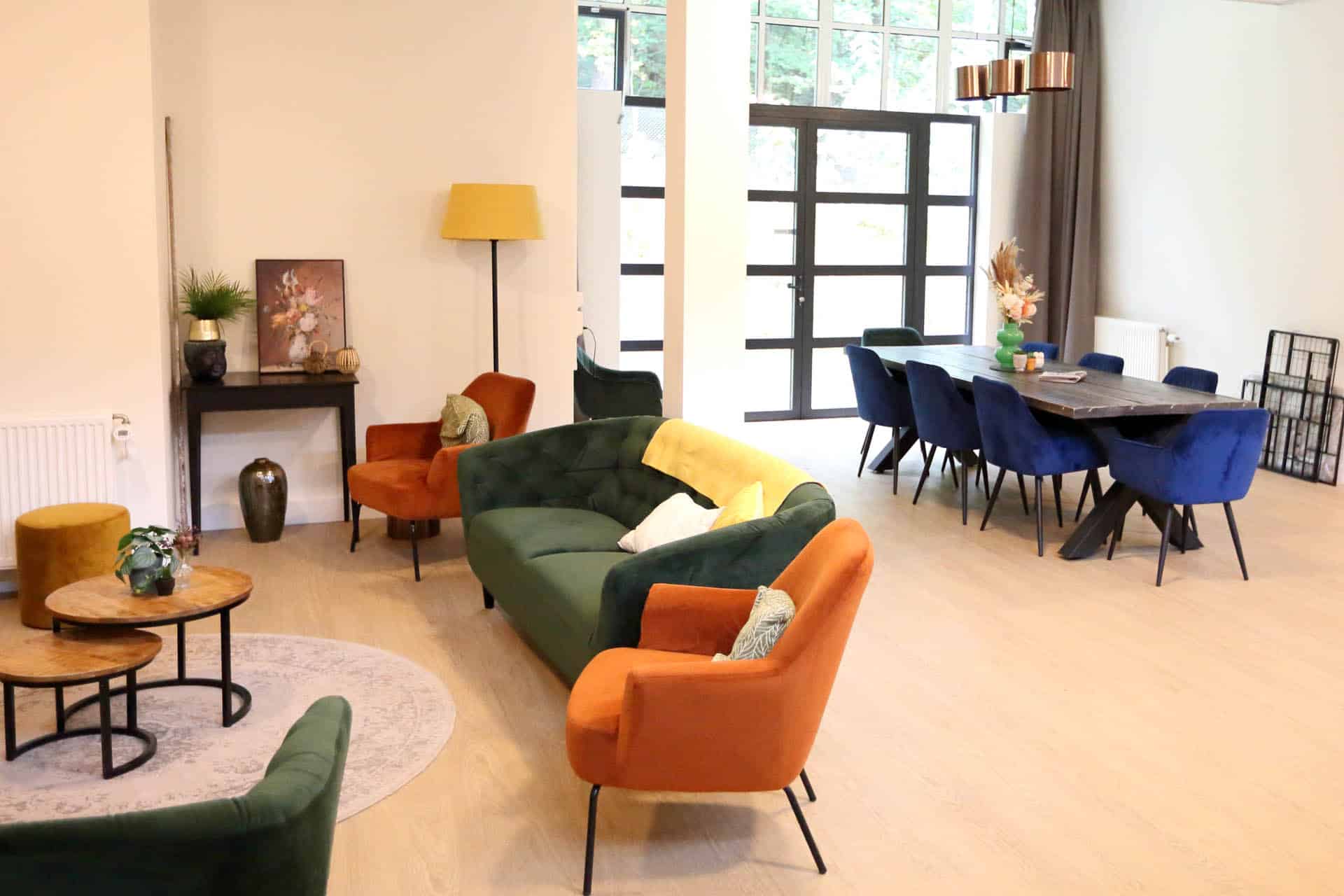 Gezamenlijke woonkamer met kleurrijke fauteuils, banken en een lange eettafel.